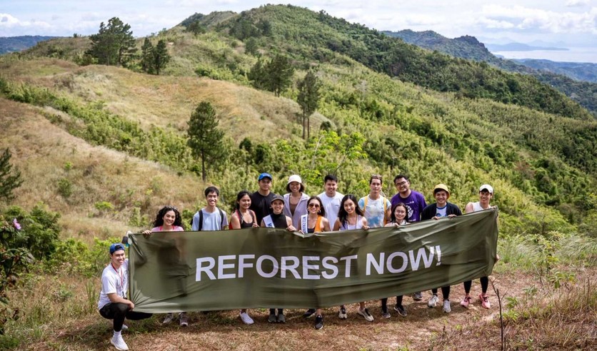 Activists with a banner saying "Reforest Now" in front of green hills